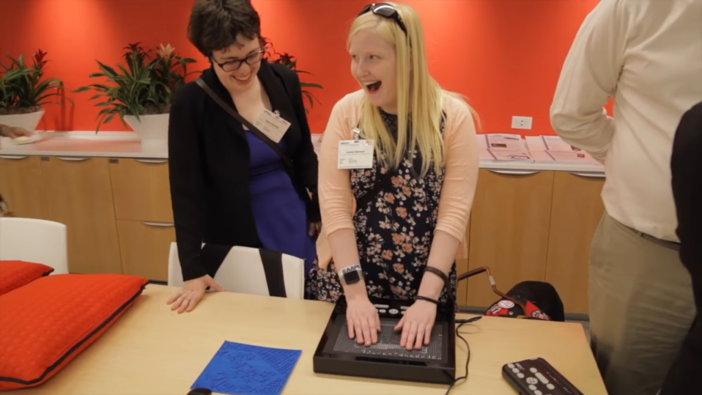 A young woman uses a new Braille device while another woman looks on at a youth advocacy workshop hosted by Verizon and Deafblind Citizens Action.